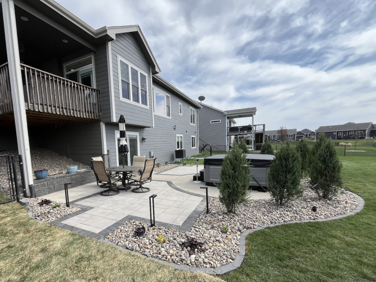 Paver patio with charcoal border, river rock perimeter, arborvitae privacy screen, and Kichler landscape lighting in Iowa