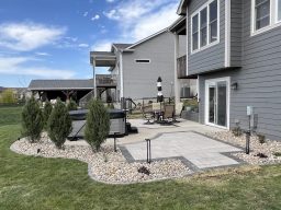 Paver patio with charcoal border, river rock perimeter, arborvitae privacy screen, and Kichler landscape lighting in Iowa