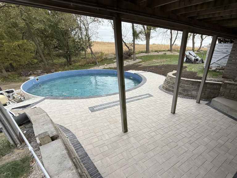 Paver patio with integrated drainage system installed alongside residential pool in Fort Dodge, Iowa