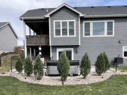 Paver patio with charcoal border, river rock perimeter, arborvitae privacy screen, and Kichler landscape lighting in Iowa